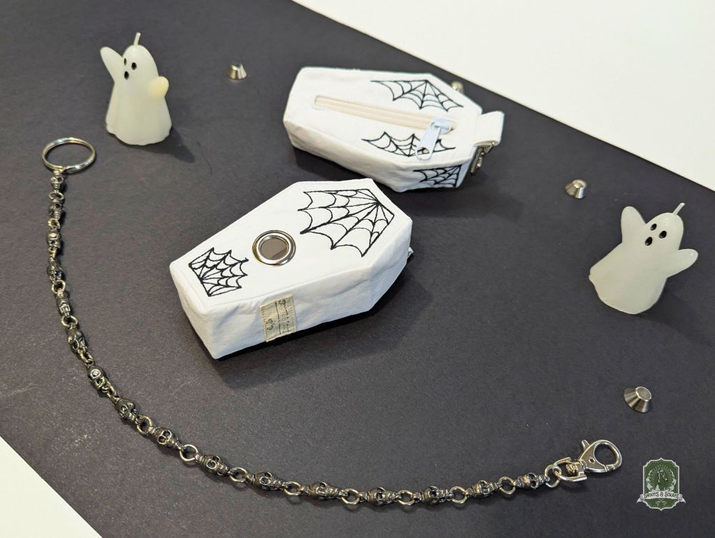 Two white coffin-shaped containers with spider web designs on a dark surface, surrounded by ghost figurines.