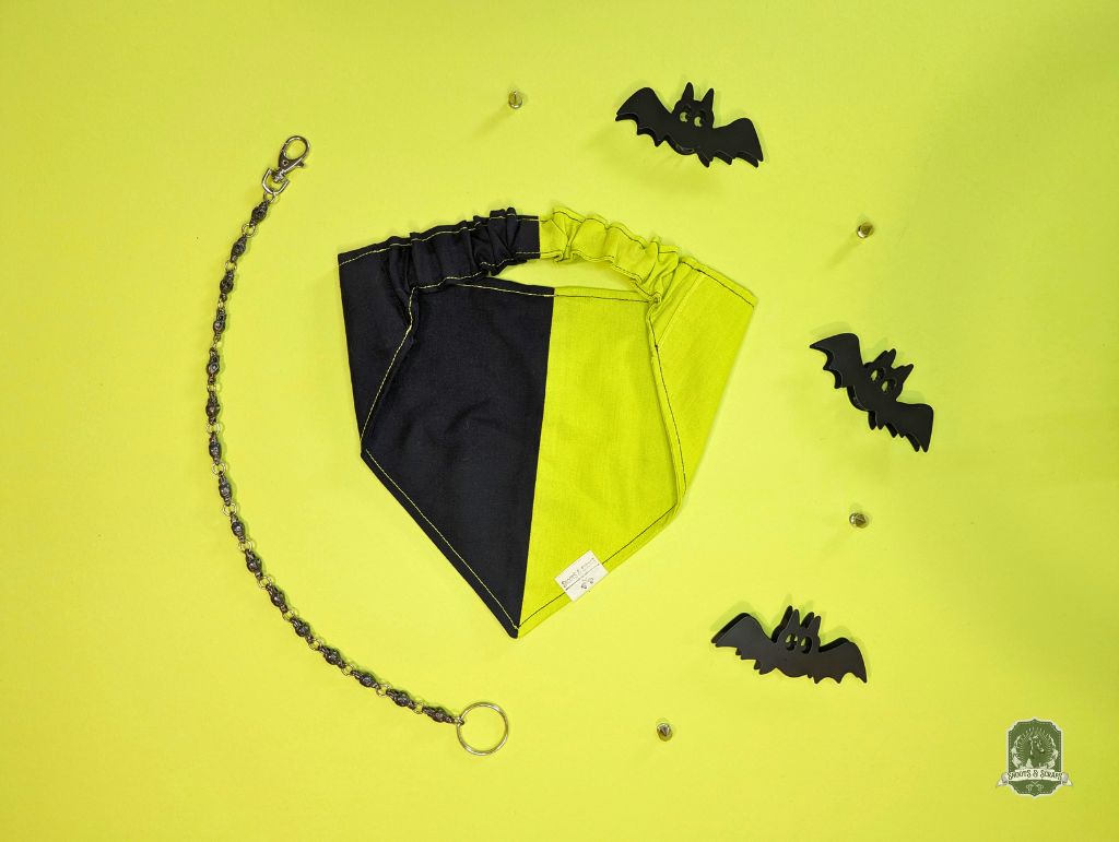 Black and acid yellow dog bandana with a chain on a yellow background with black bat decorations.