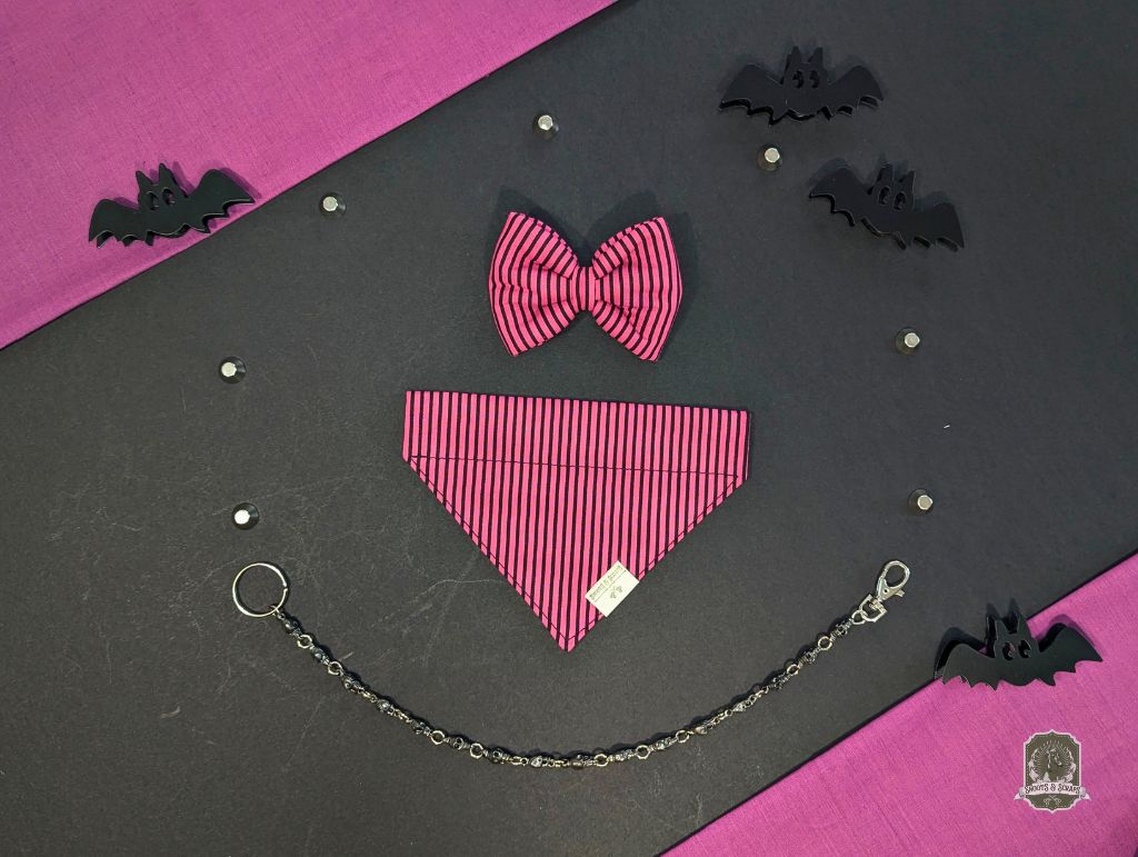 Pink bow tie and matching dog bandana with a chain on a black and pink background with bat decorations.