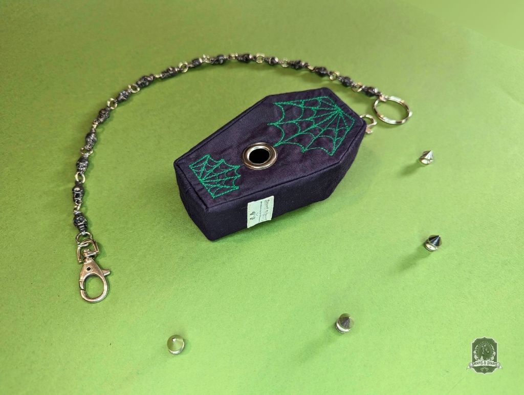 Black coffin-shaped dog poop bag holder with green spider web design on a green background