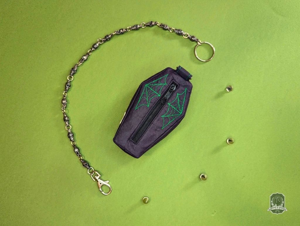Black coffin-shaped dog poop bag holder with green spider web design on a green background