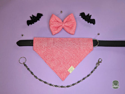 Pink zebra print pet bow tie  set with matching dog bandana on a black leather collar with a pastel pink background and decorative chain.