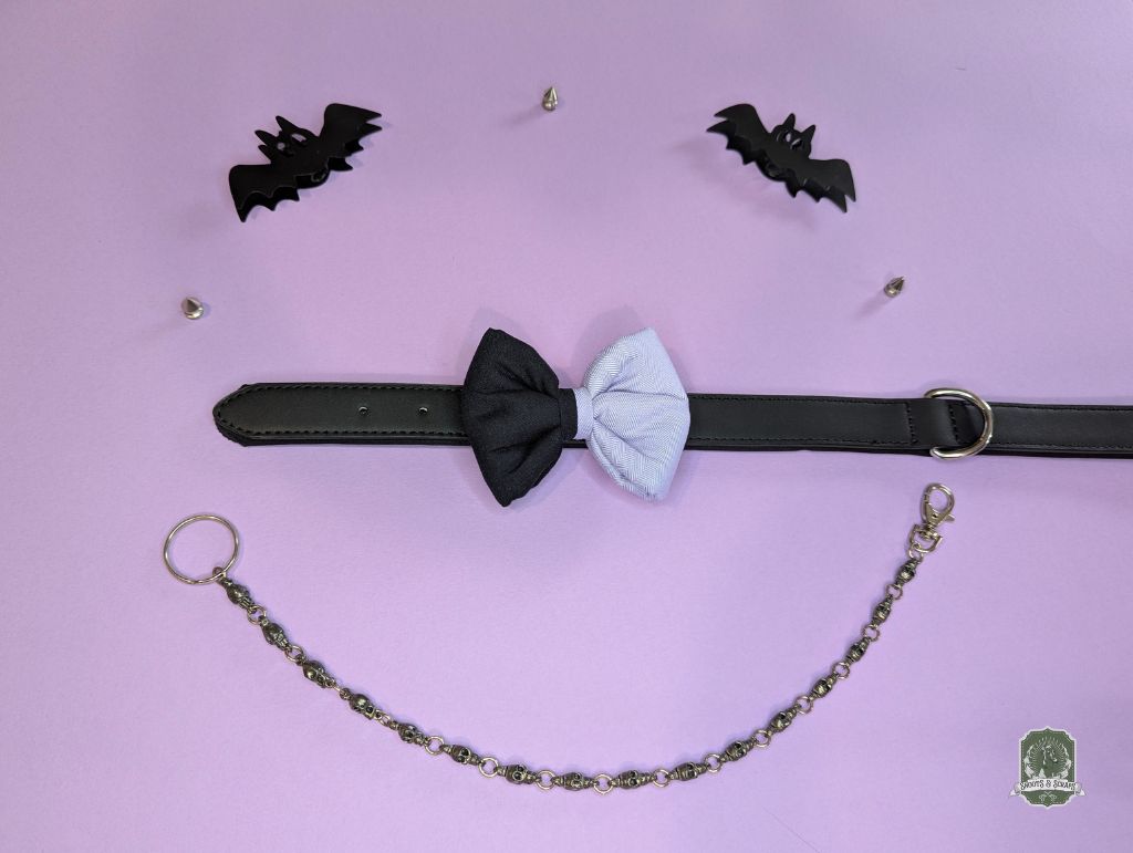 Black and lilac dog bow tie with a chain and bat-shaped accessories on a pink background