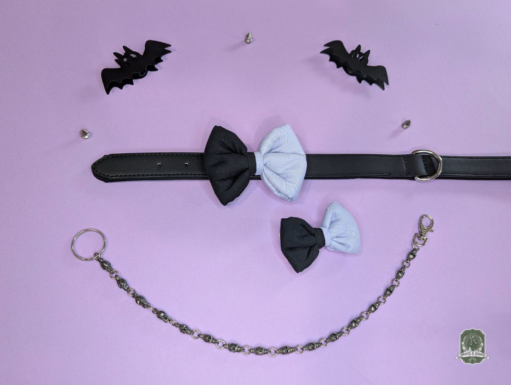 Black and lilac dog bow tie with a chain and bat-shaped accessories on a pink background