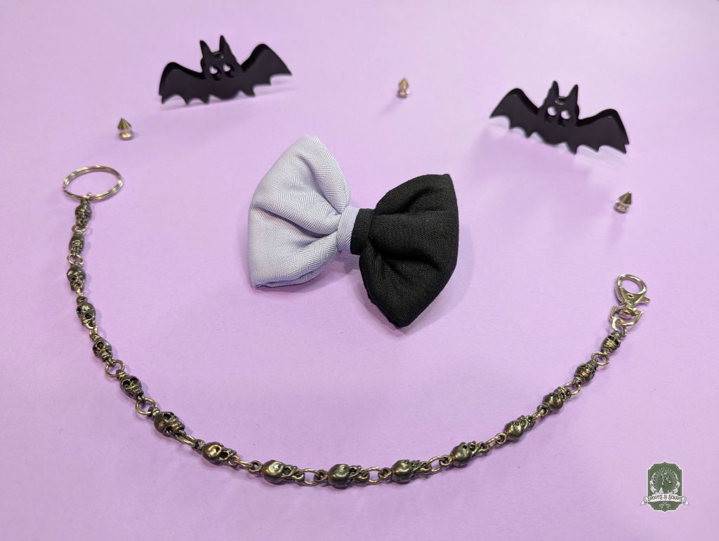 Black and lilac dog bow tie with a chain and bat-shaped accessories on a pink background