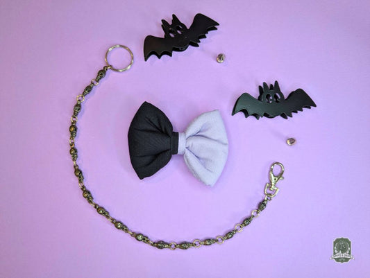 Black and lilac dog bow tie with a chain and bat-shaped accessories on a pink background