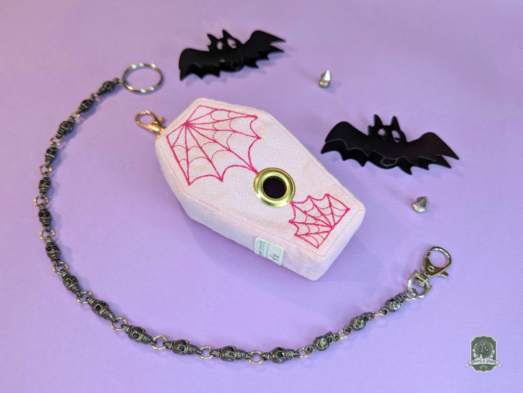 Coffin-shaped dog poo bag holder with spider web design on a pink background