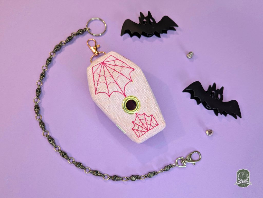 Coffin-shaped dog poo bag holder with spider web design on a pink background