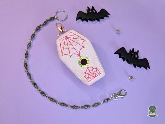 Dog poop bag holder with coffin design, spider webs, and bats on a purple background