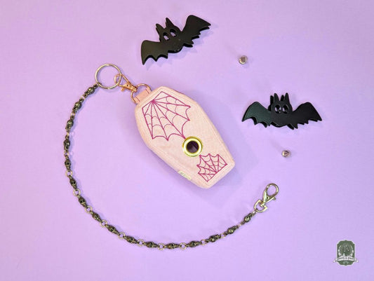 Coffin shaped dog poo bag dispenser with spider web design and black bats on a purple background