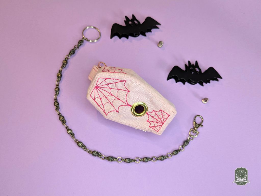 Coffin-shaped dog poo bag holder with spider web design on a pink background