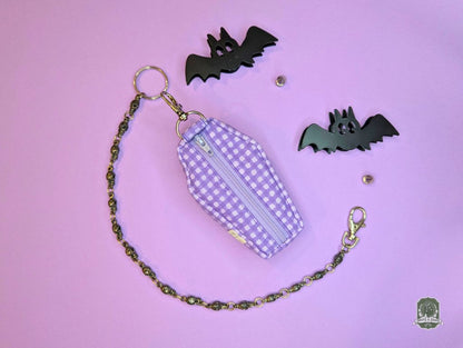 Purple checkered coffin-shaped poop bag holder dispenser pouch with chain on a pink background with black bat decorations.