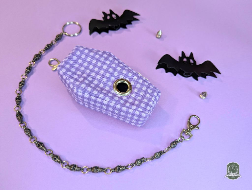 Checkered poop bag dispenser coffin shaped, with chain on a purple background with black bat decorations
