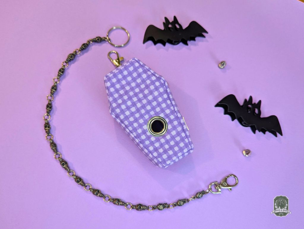 Purple checkered coffin-shaped poo bag holder with chain on a purple background