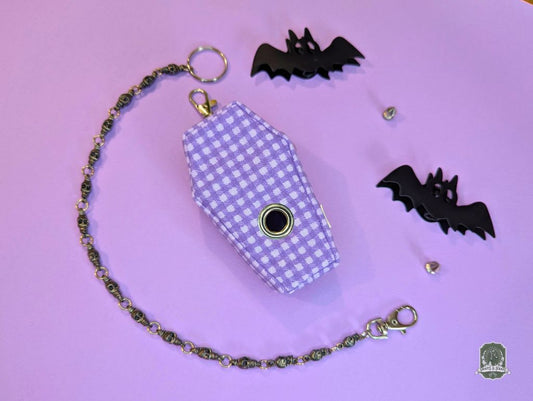 Purple checkered coffin-shaped poo bag holder with chain on a purple background