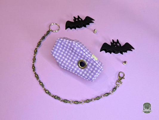Coffin shaper poop bag dispenser purple and white checkered bag with a chain on a pink background