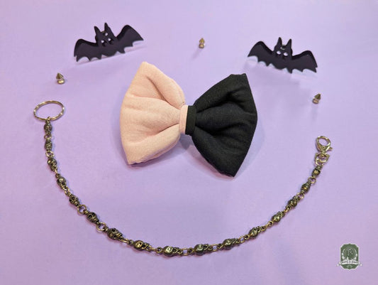 Black and light pink pet bow tie with decorative chain on a purple background with small black bats.