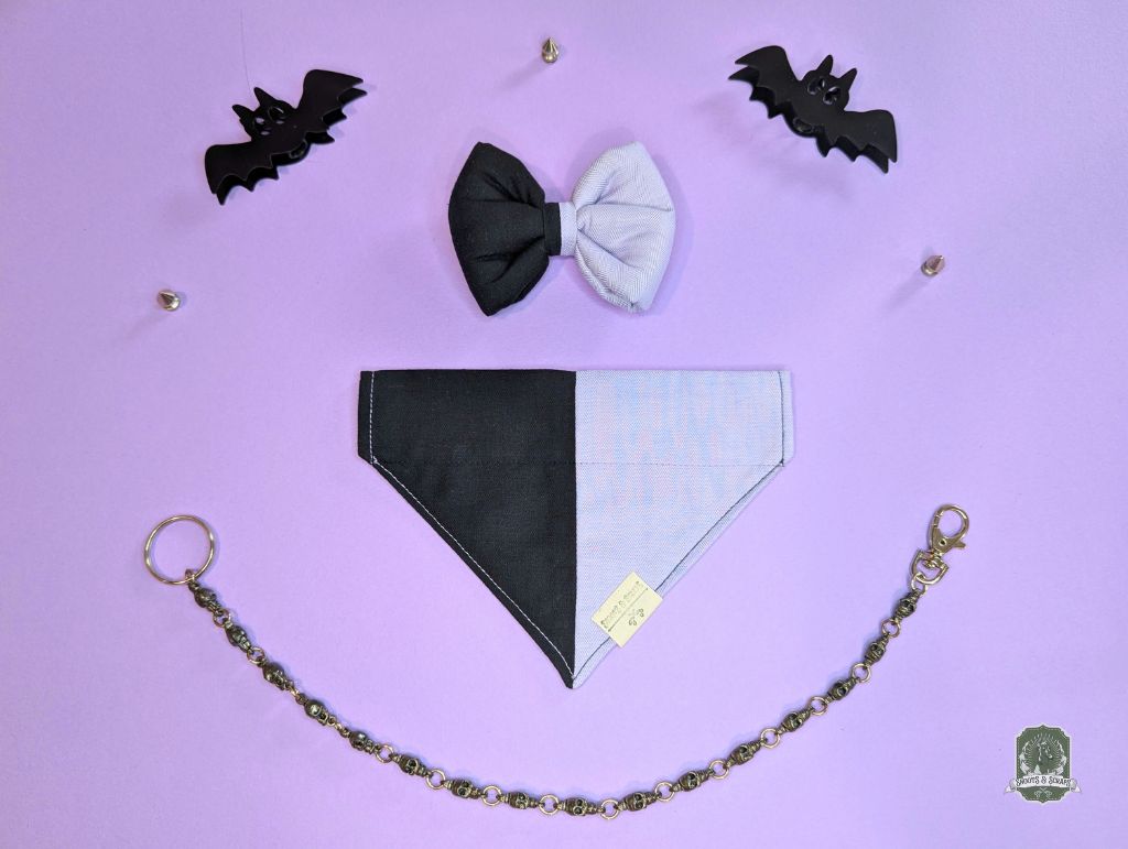Black and lilac dog bandana with matching pet bow tie and black bat decorations on a purple background.