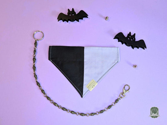 Black and lilac dog bandana with chain on a purple background with bat decorations.