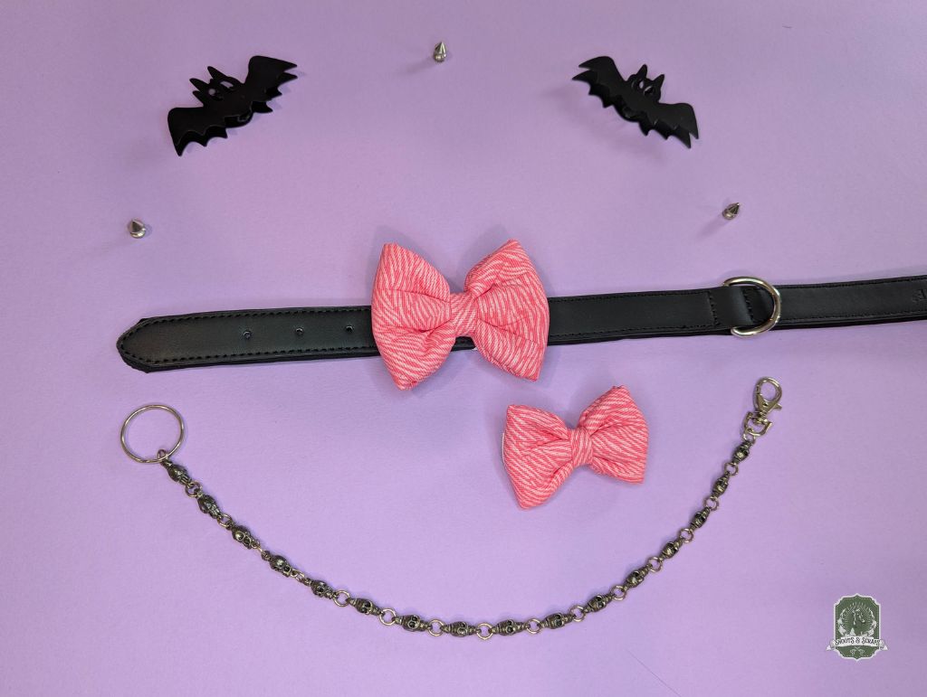 Pink zebra print pet bow ties displayed on a black leather collar with a pastel pink background and decorative chain.