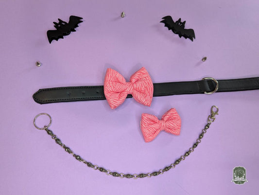 Pink zebra print pet bow ties displayed on a black leather collar with a pastel pink background and decorative chain.