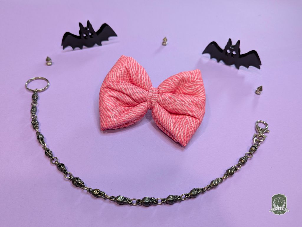 Pink zebra print dog or cat bow tie displayed on a pastel pink background and decorative chain and bats figurines
