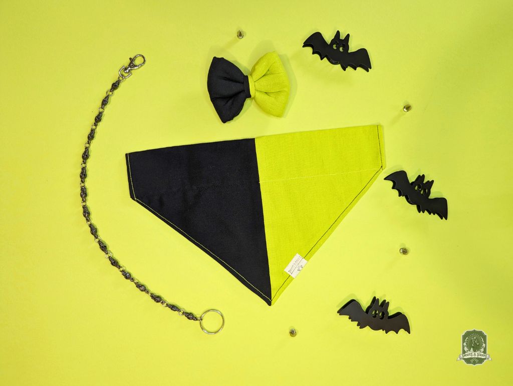 Halloween-themed pet accessories including a bandana, bow tie, and  decorative bats on a yellow background.