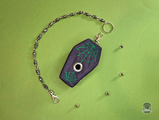 Black coffin-shaped dog poop bag holder with green spider web design on a green background