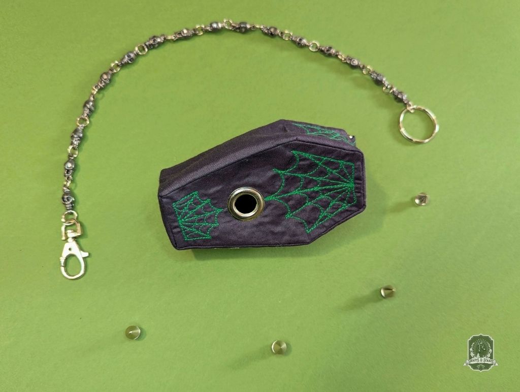 Black coffin-shaped dog poop bag holder with green spider web design on a green background