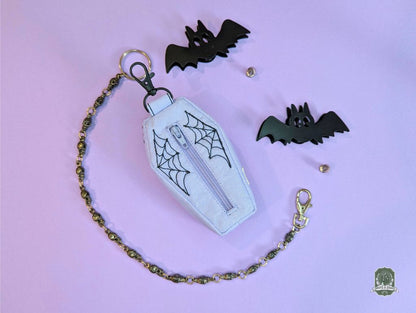 lilac coffin shaped poop bag holder with black embroidered spiderwebs on a pastel pink background