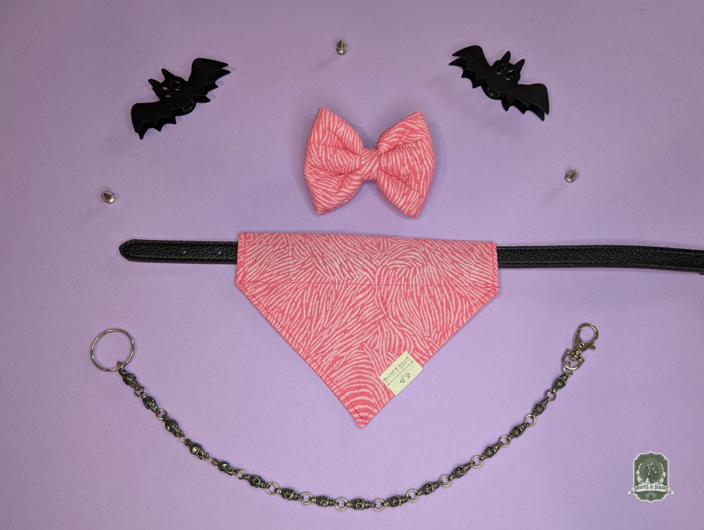 Pink dog bow tie and bandana set displayed with black leather collar on a purple background